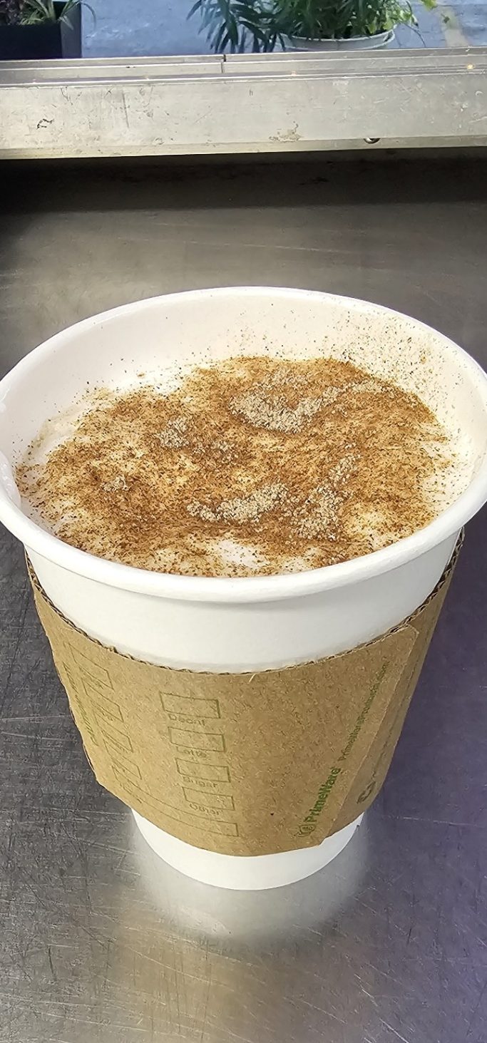 White paper cup filled with coffee, topped with foam and a sprinkle of cinnamon.