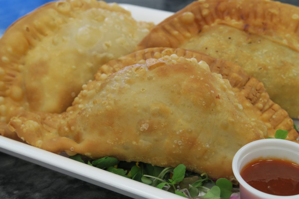 Three golden-brown empanadas on a plate with a small cup of dipping sauce.