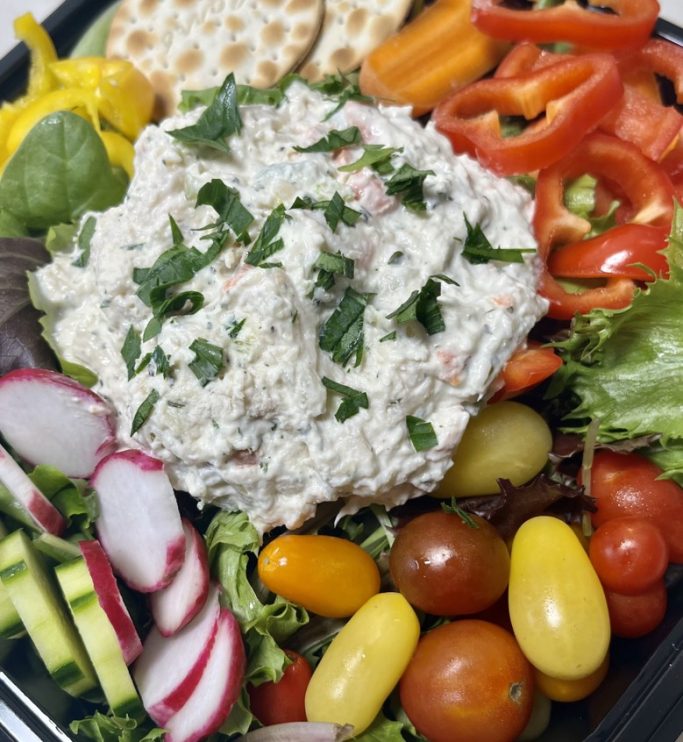 A colorful vegetable platter with a creamy dip and crackers.
