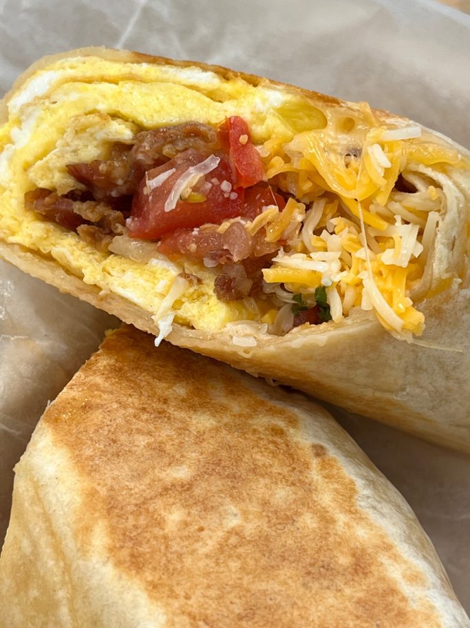 Breakfast burrito with egg, sausage, cheese, and diced tomatoes, partially sliced.