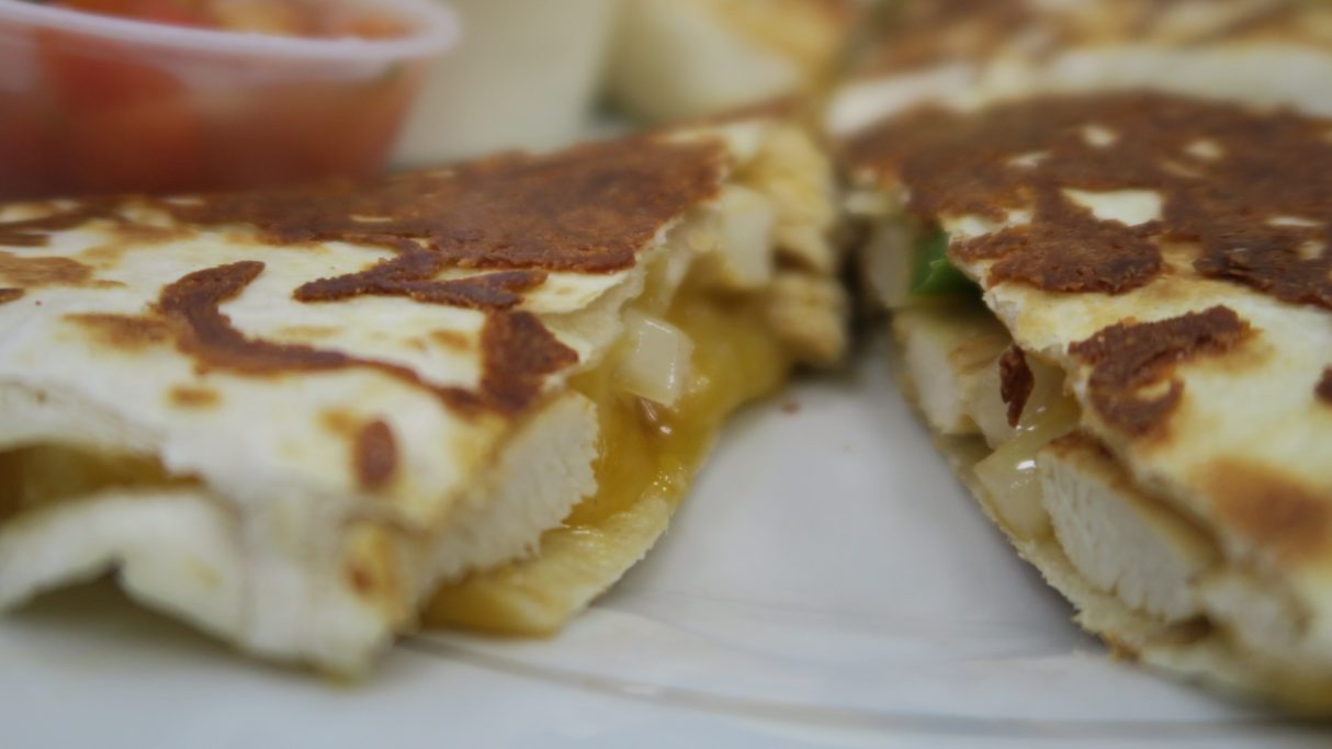 Jerk Chicken quesadillas filled with melted cheese and chunks of chicken, served with salsa, sour cream.