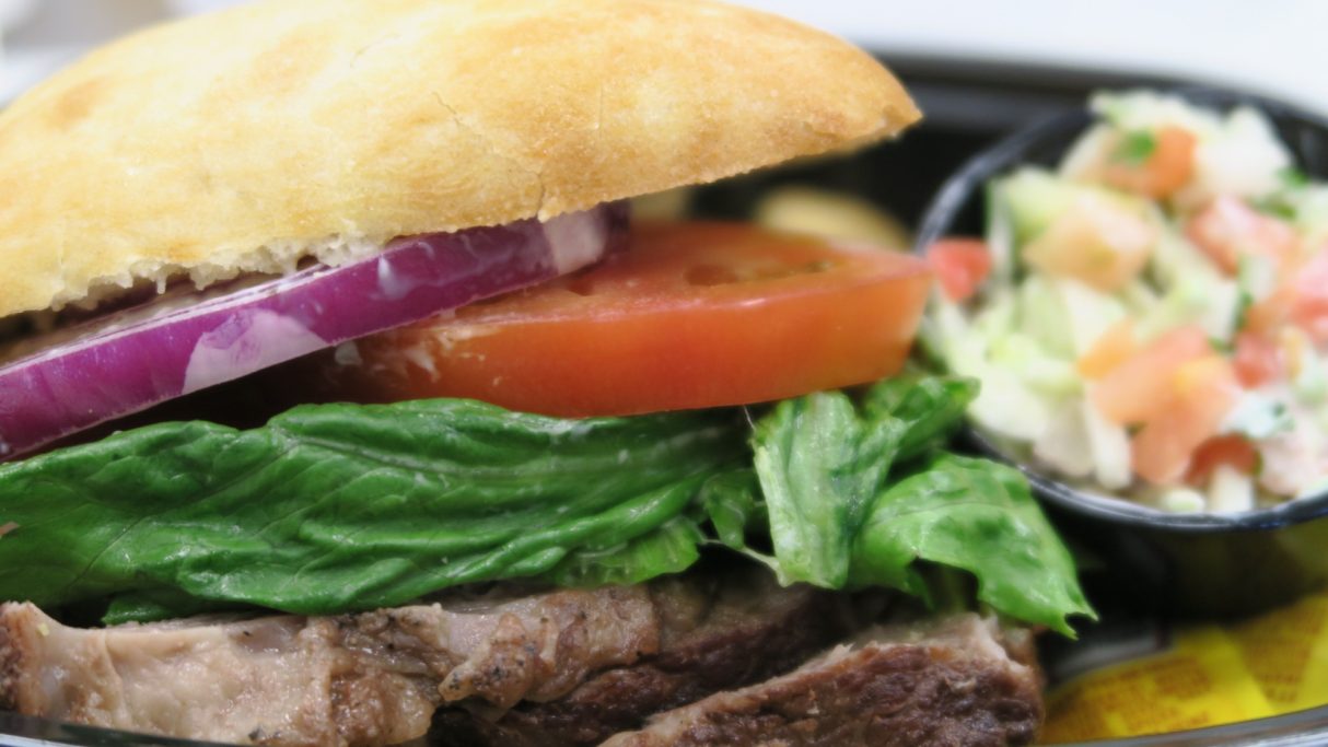 A sandwich with lettuce, tomato, onion, and grilled meat, served with a side salad.