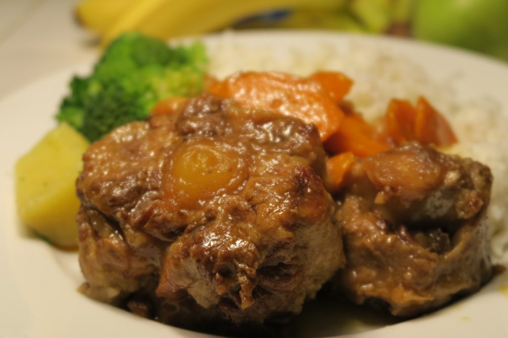 Plate of rice with braised meat, broccoli, carrots, and sliced fruit.